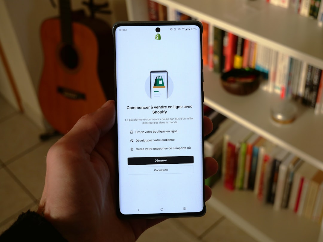 a hand holding a smartphone displaying the welcome screen of the Shopify app. The app interface is in French and invites users to start selling online with Shopify. It presents three options: Create your online store, Grow your audience, and Manage your business from anywhere. Two buttons are visible at the bottom of the screen: Start and Login.